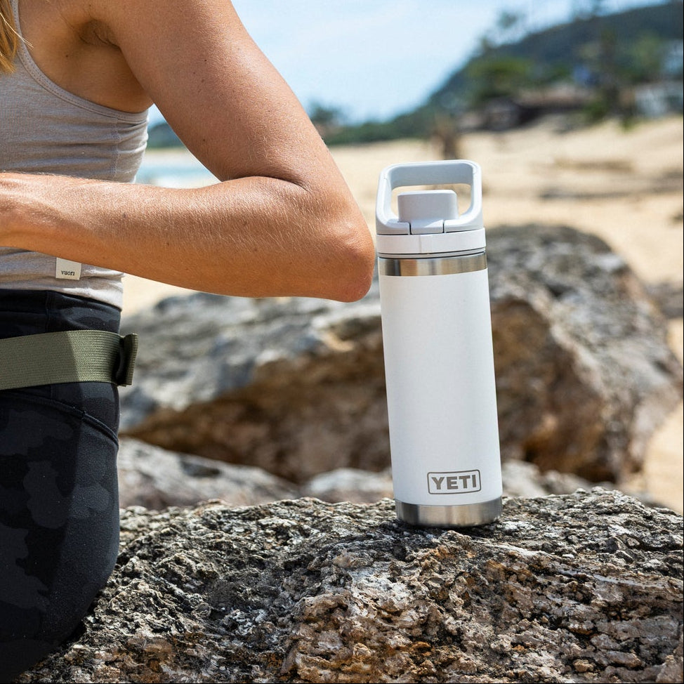 Woman sitting on a rock by the beach with a YETI water bottle.