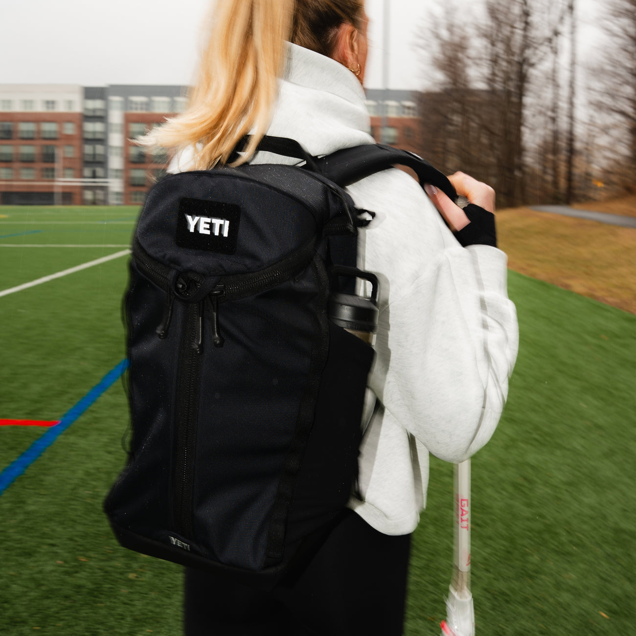 Person wearing a black YETI backpack on a sports field