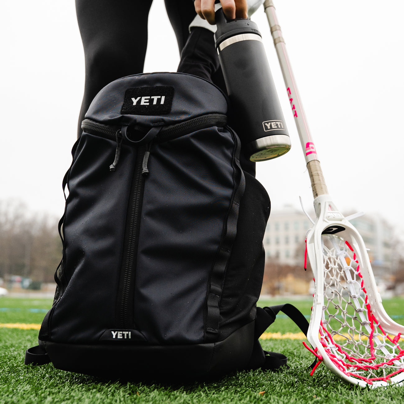 Black YETI backpack with a lacrosse stick and ball on grass