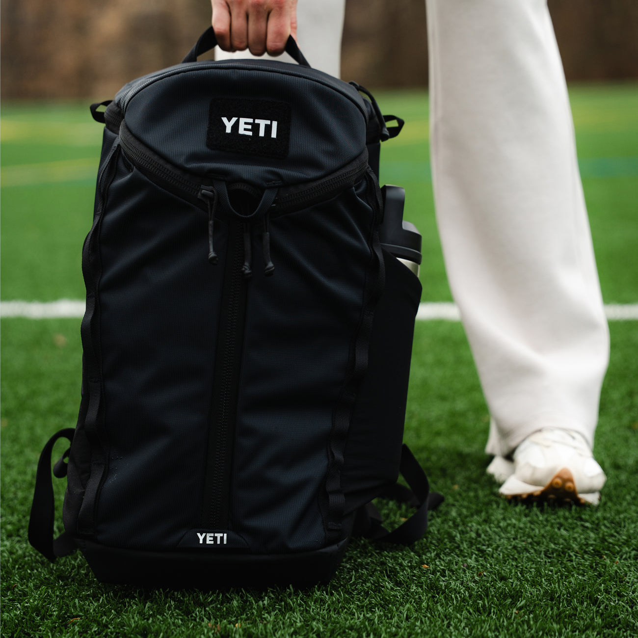 Black YETI backpack on grass with a person wearing white pants and shoes.