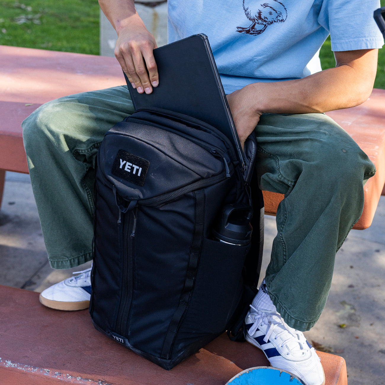 Person sitting on a bench with a YETI backpack and laptop