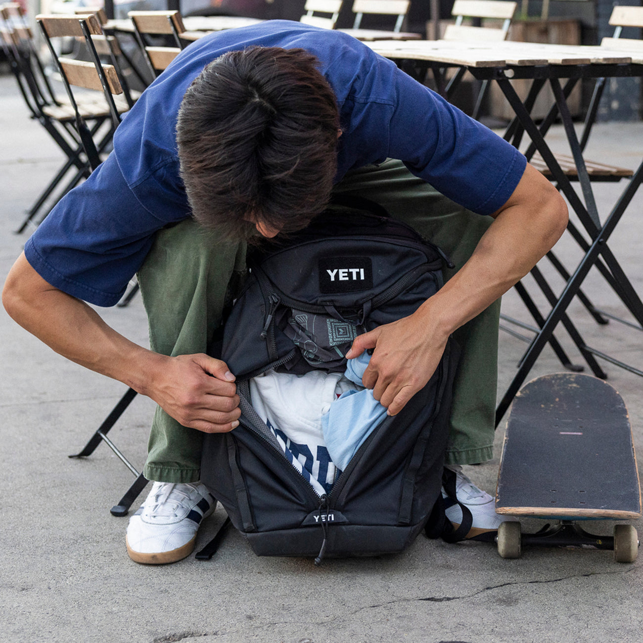 Person opening a YETI backpack outdoors with tables and chairs in the background