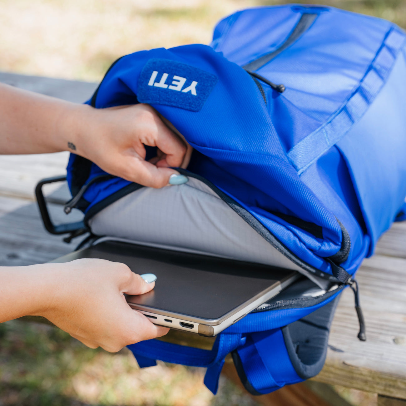 Blue YETI backpack with a laptop being placed inside, on a wooden surface.