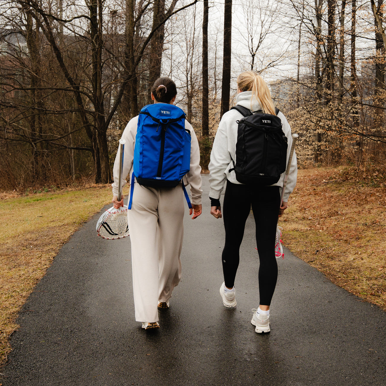 Two people walking on a path in a forested area with YETI backpacks.